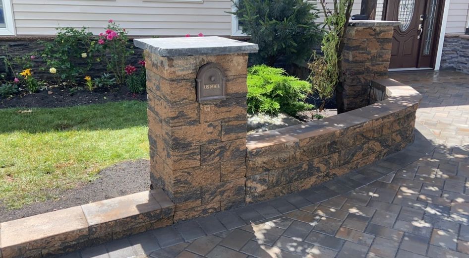 Stone mailbox pillar and low retaining wall beside a paved driveway and house entrance