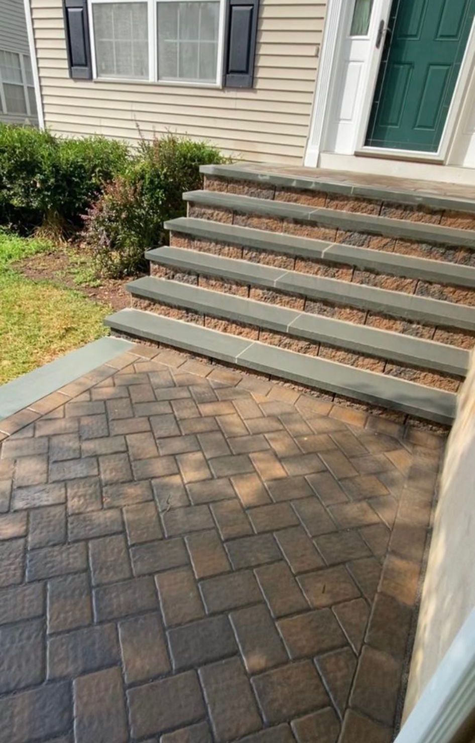 Front steps with gray risers leading to a green door beside a brick paver walkway.