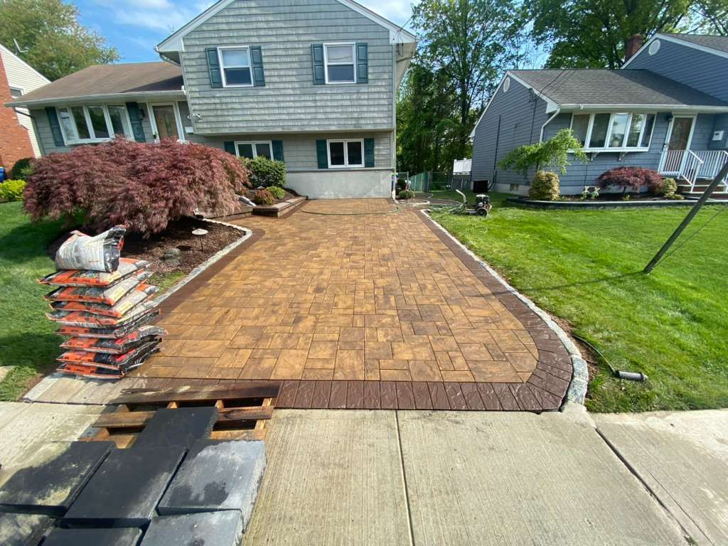 Driveway being paved with tan pavers beside a suburban house and lawn