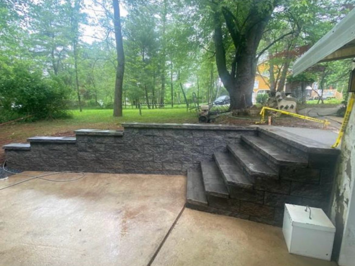 Stone retaining wall with steps leading to a wooded yard and patio area