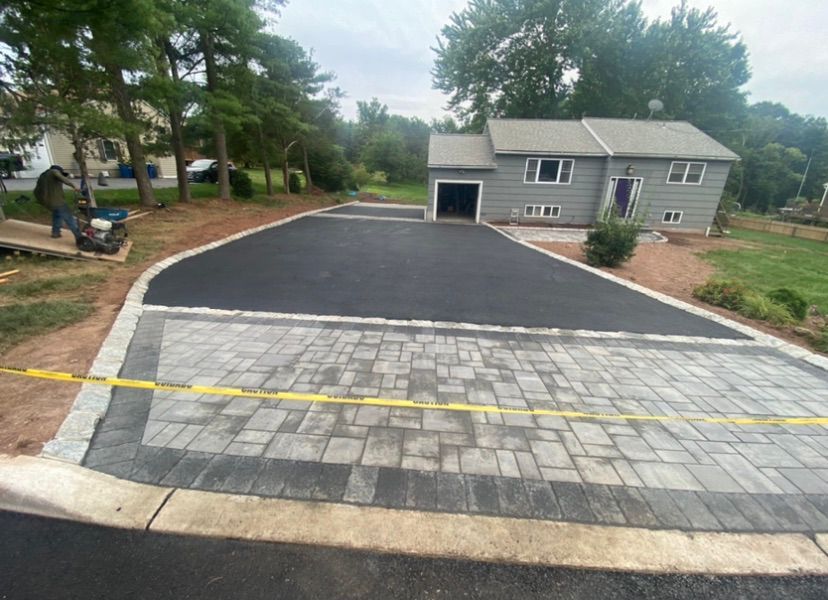 Freshly paved driveway with yellow caution tape in front of a gray house and garage.