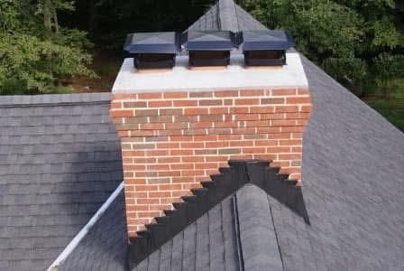 Brick chimney with three black caps on a gray shingled roof.