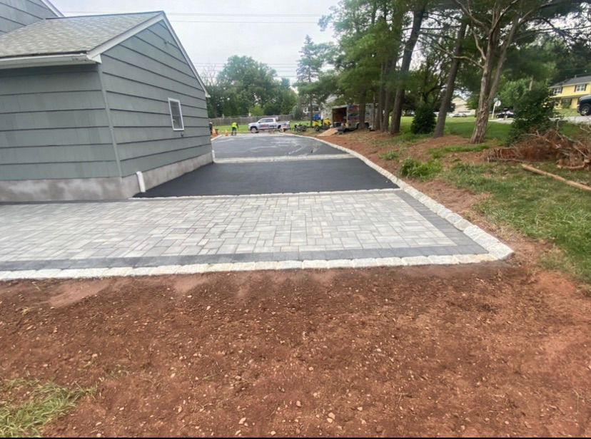 Paved driveway beside a gray house, with fresh landscaping and a road in the background.