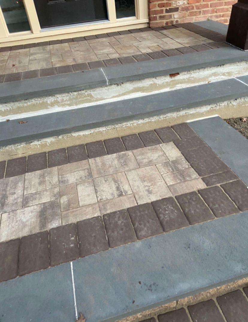 Brick walkway with gray concrete steps leading to a building entrance.