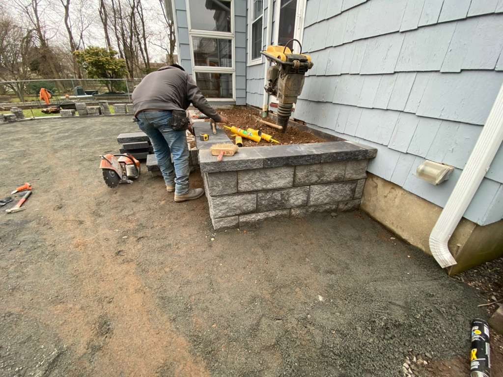 Worker repairing a stone porch beside a gray house, with tools and yellow foam on top.