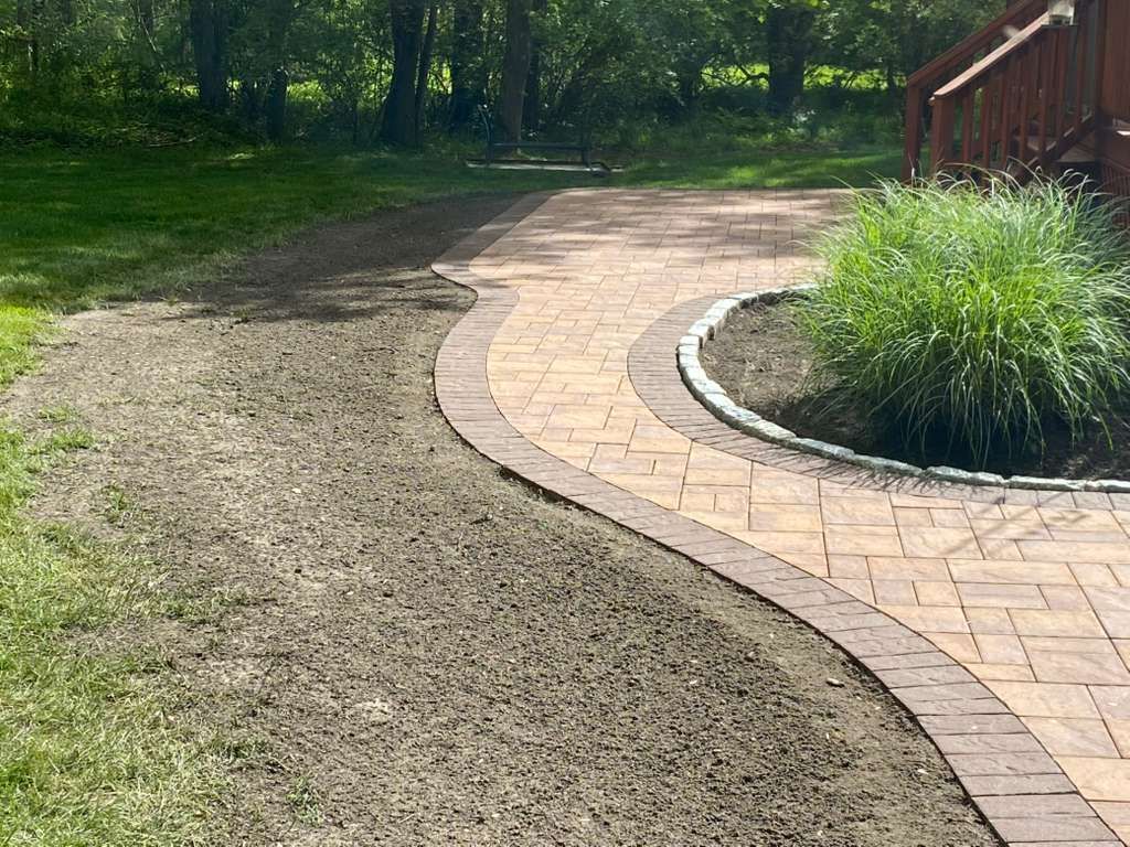 Curving brick walkway beside a gravel path and green garden beds in a sunny yard