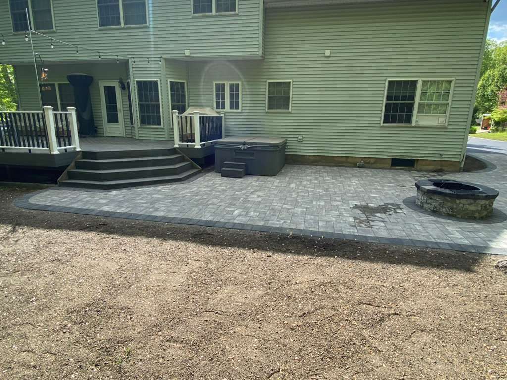Backyard patio with steps, gray seating, and round fire pit beside a house