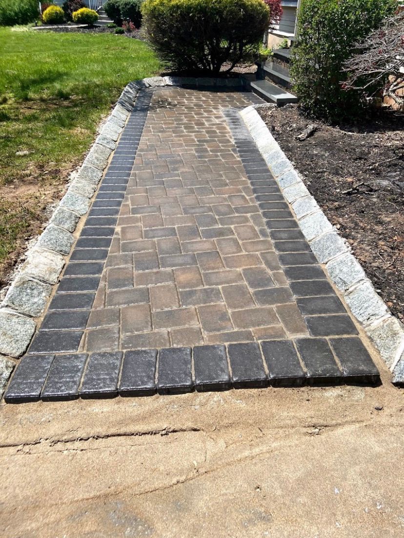 Brick walkway bordered by white stones leading through a garden lawn toward a shrub