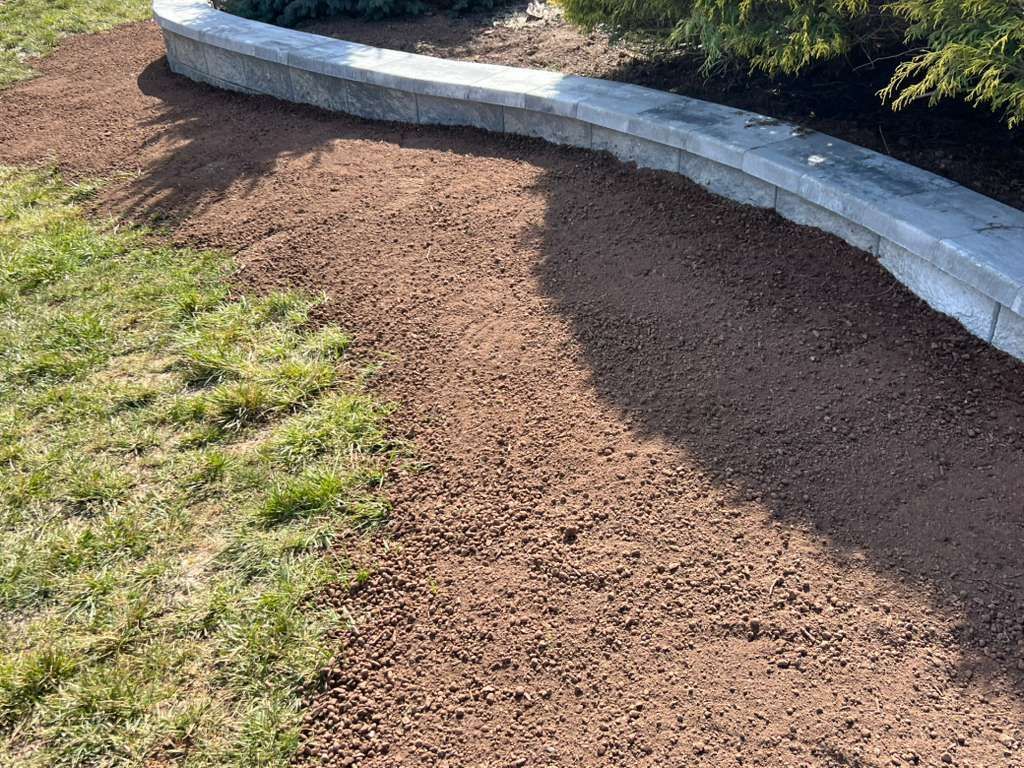 Curved stone retaining wall beside a mulched garden bed and patchy grass in sunlight