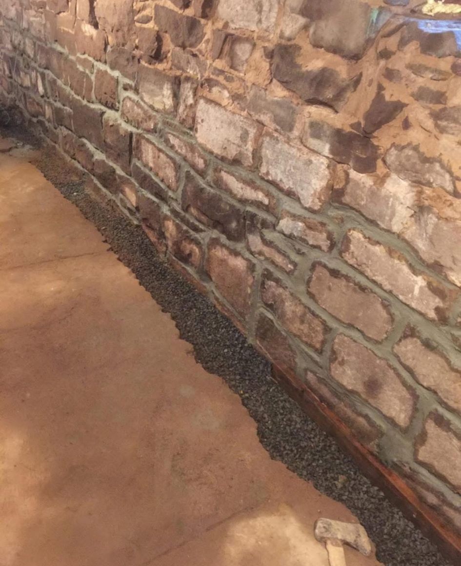 Stone wall beside a concrete floor with a narrow strip of gravel along the base