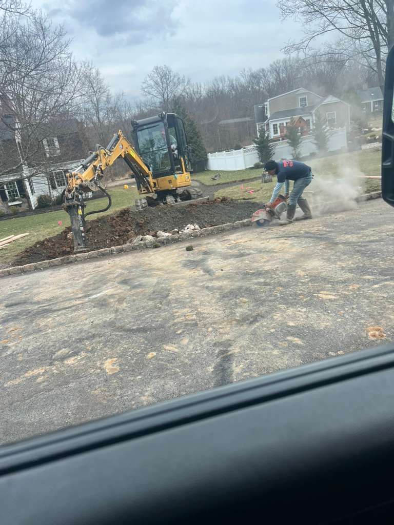 Roadwork scene with a backhoe and two workers shoveling on a residential street
