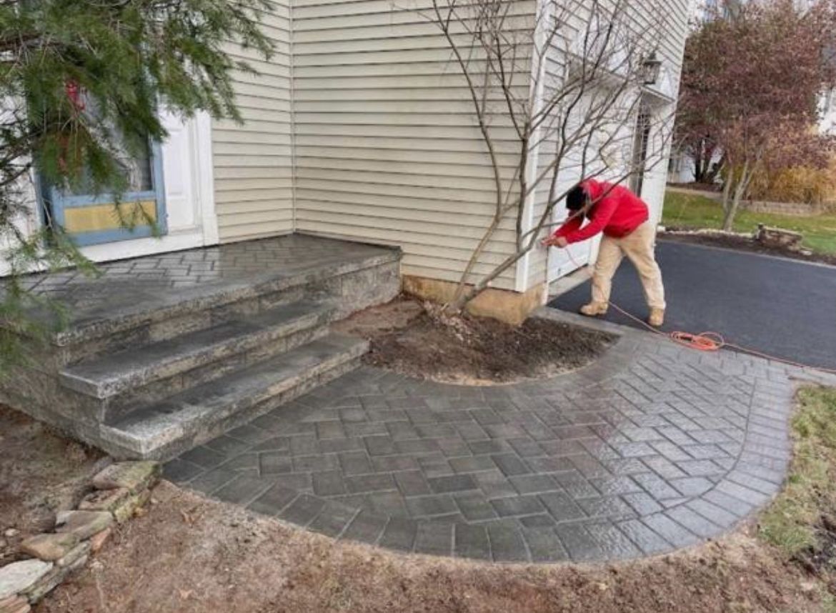 Person raking leaves beside a house entrance and paved walkway.