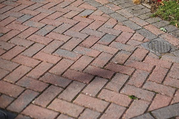 Brick paved walkway with a dark stain and a drain grate near the edge