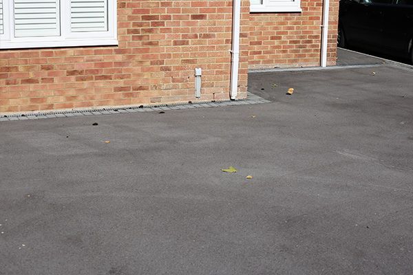 Brick house wall beside a paved driveway with a garage entrance and white shuttered window