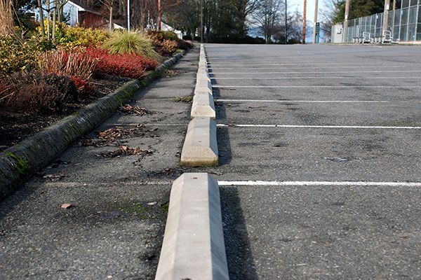 Empty parking lot with concrete wheel stops and landscaped curb along the side