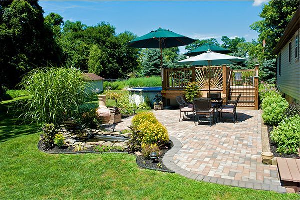 Backyard patio with stone walkway, outdoor seating, umbrellas, and lush green landscaping
