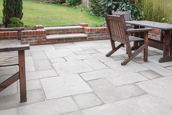 Patio with large stone pavers, wooden table and chairs beside a low brick garden wall