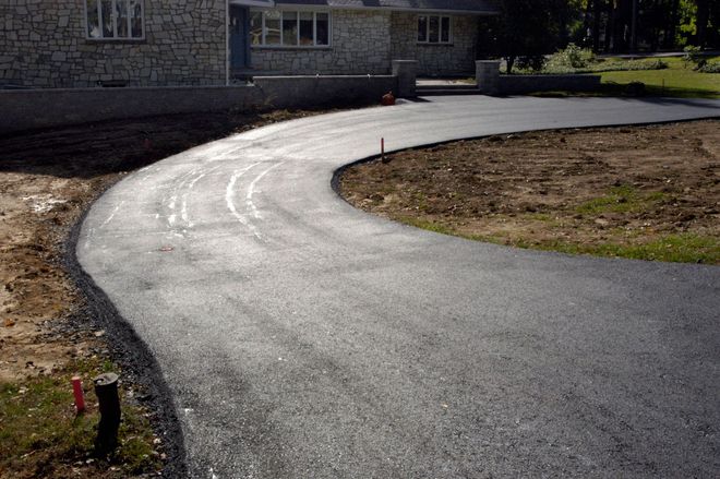 Curved freshly paved driveway leading to a house, with a dirt edge and lawn beside it.