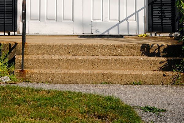Front steps of a white house with tan concrete stairs, black railings, and grass in the foreground