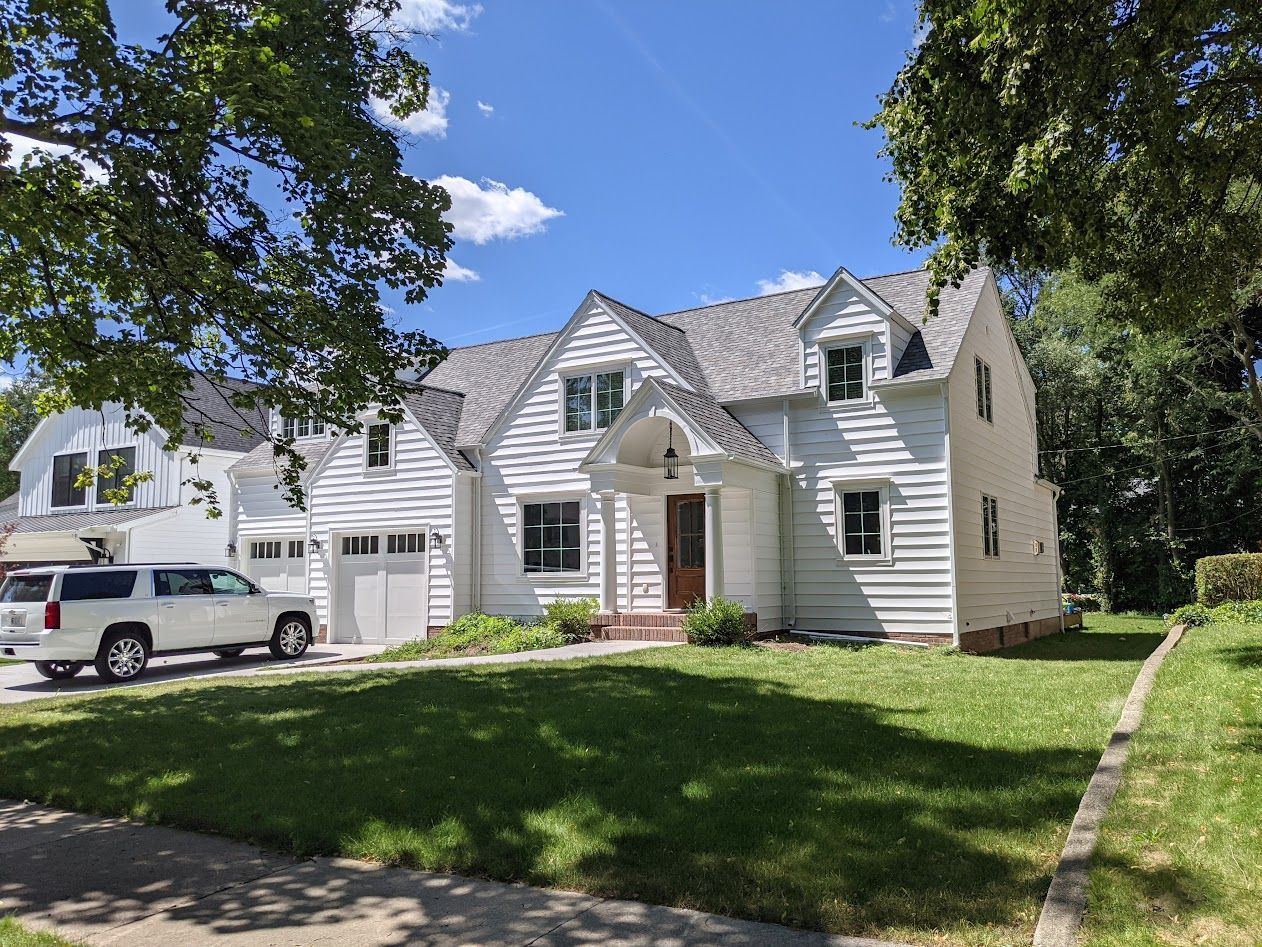 White house with a gray roof and green lawn on a sunny day; a white SUV is parked in front.