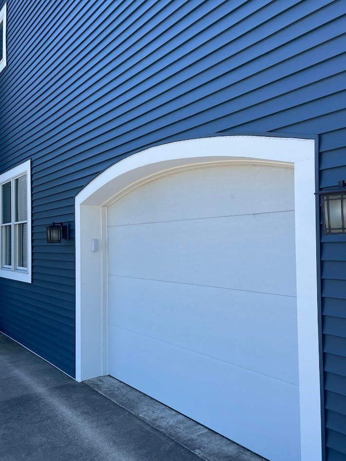 White garage door with arched top and white trim, set in a blue clapboard-sided building.