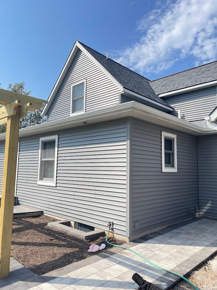 Gray house with siding, roof, and white window trim; blue sky background.