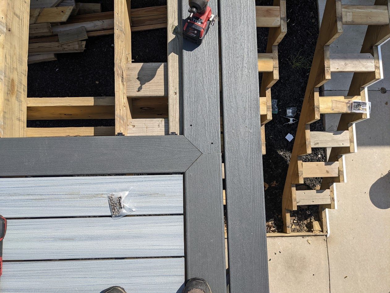 Deck construction: Composite decking laid over wooden frame; worker using power tool.