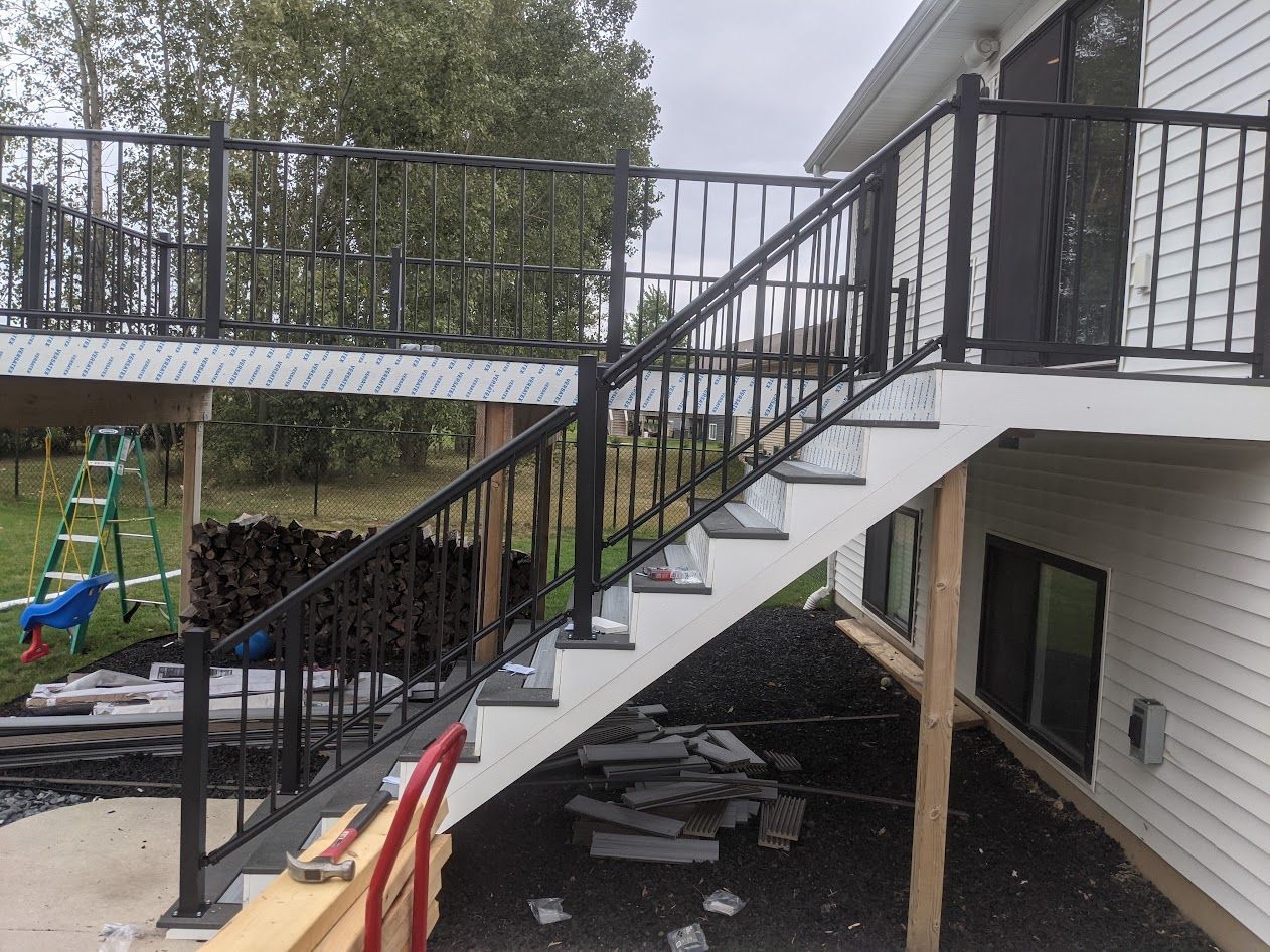 A black railed staircase leading to a white deck, built on the side of a white house.