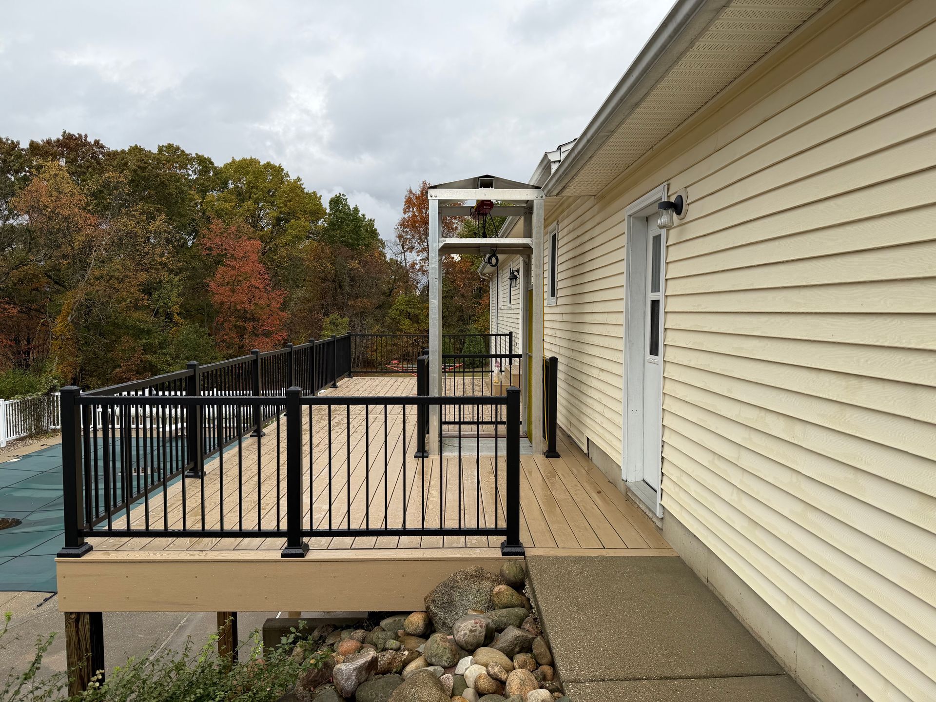 Deck with lift to house door, black railing, composite decking, and fall foliage in the background.