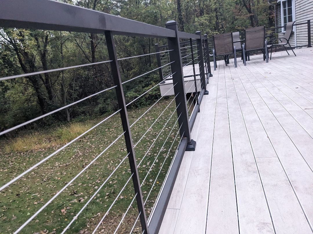 Deck with gray metal railing and cable wires, overlooking a grassy area and trees.
