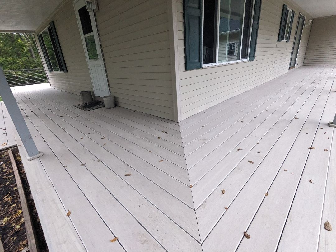 Beige deck with light-colored siding, a white door, and windows with green shutters.