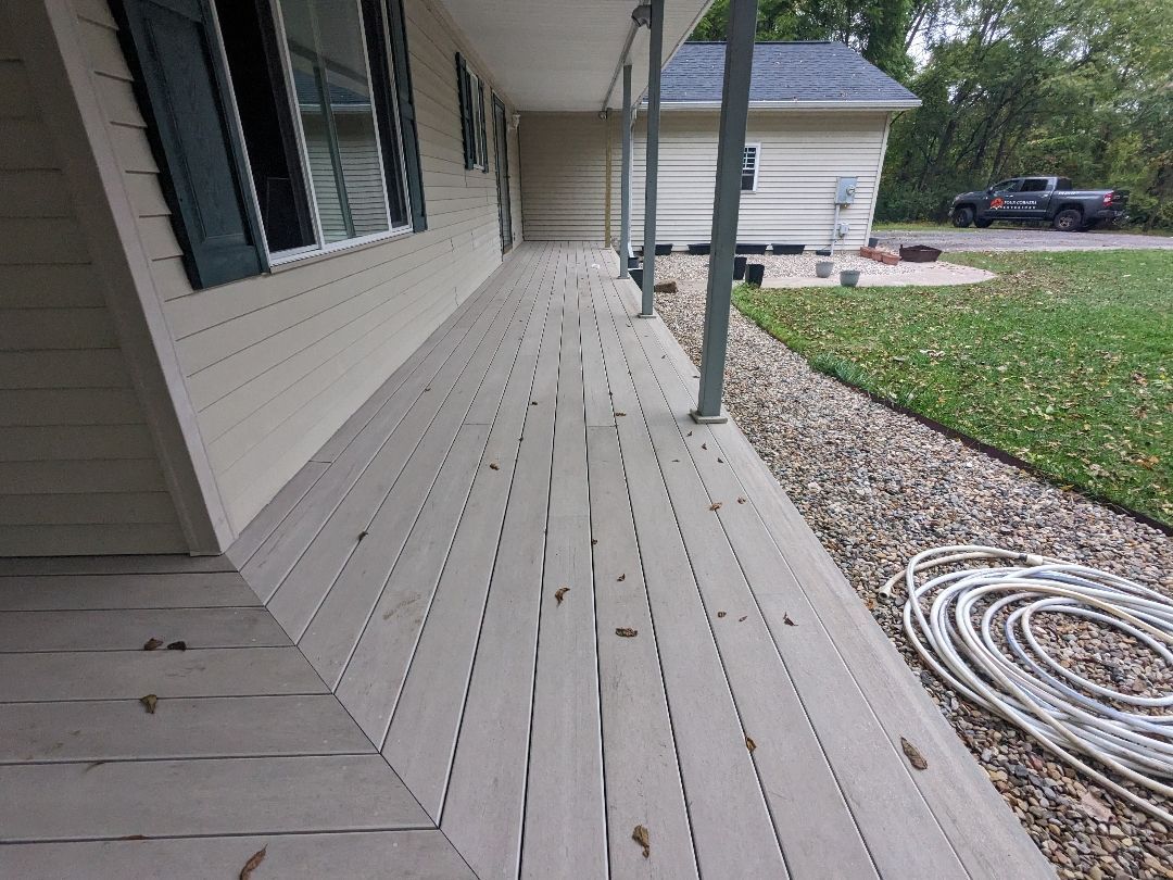 A long, weathered wooden porch extends from a cream-colored house. Cables lie on the ground near the porch's edge.