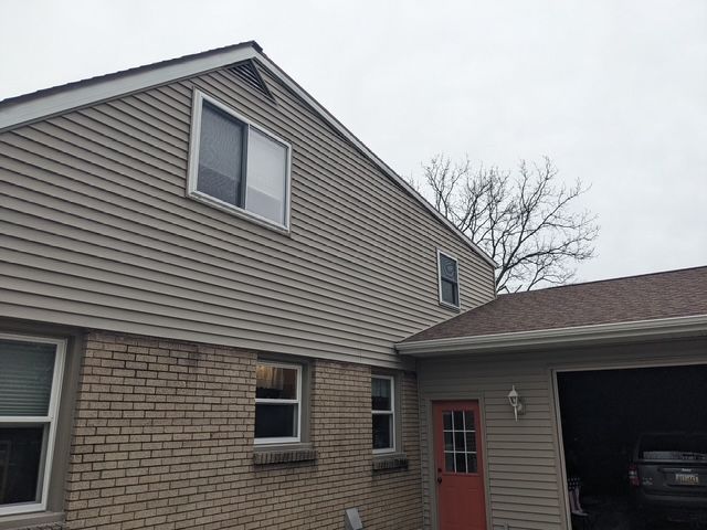 Two-story house with tan siding above brick, attached garage, and cloudy sky.