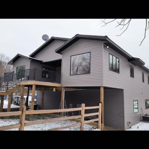 Two-story gray house with black trim and a deck, set in a snowy landscape.
