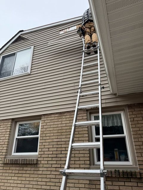Person on ladder repairing siding on a two-story brick house.