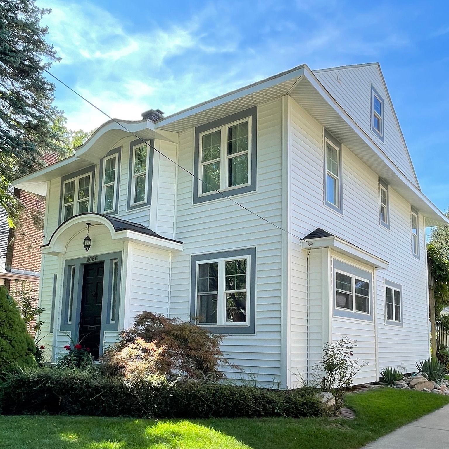 Two-story white house with gray trim, lawn, and blue sky.