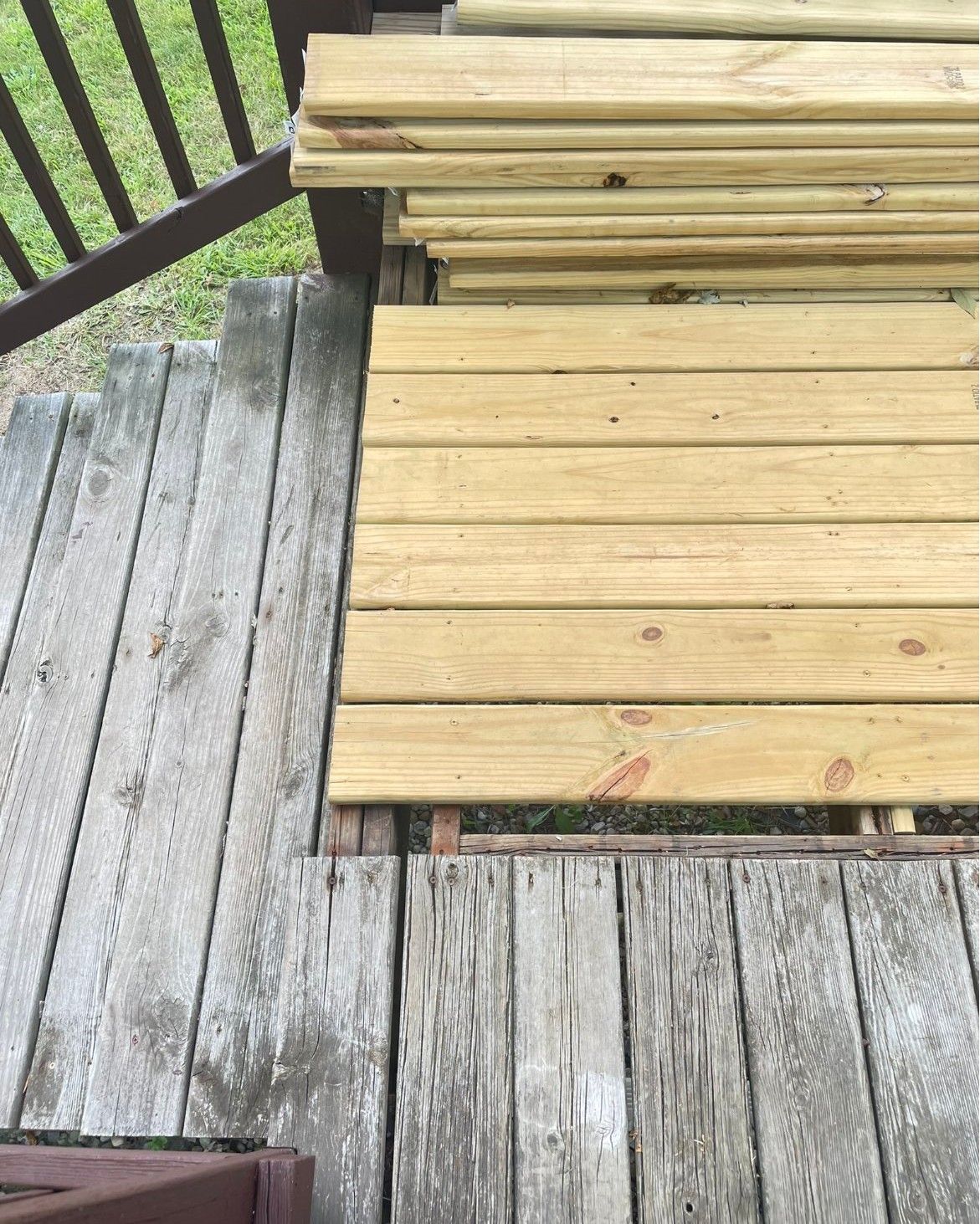 Deck with old, weathered boards beside new, golden planks. Boards stacked nearby.