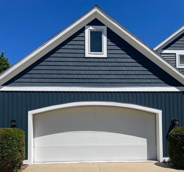 Blue-sided house with white arched garage door, gable with window, and bright blue sky.