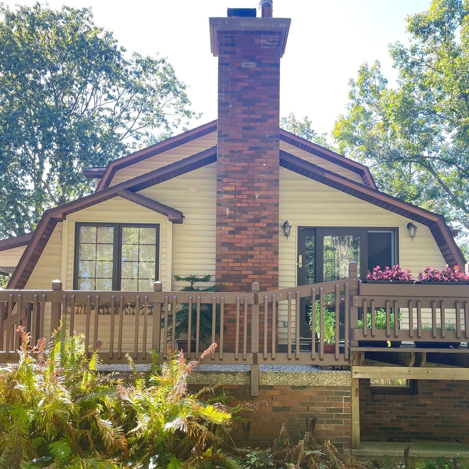 Beige house with a red brick chimney, brown deck, and trees.