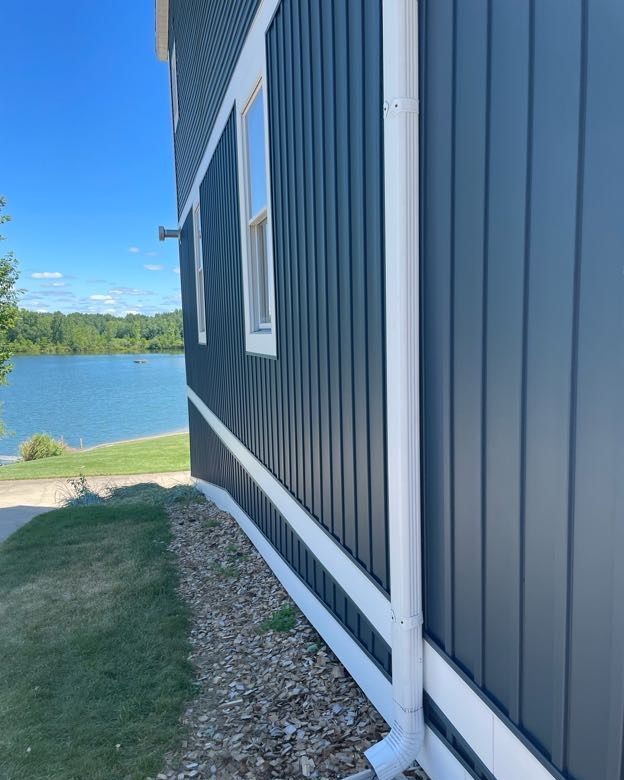 Dark blue house with white trim, overlooking a lake under a blue sky.