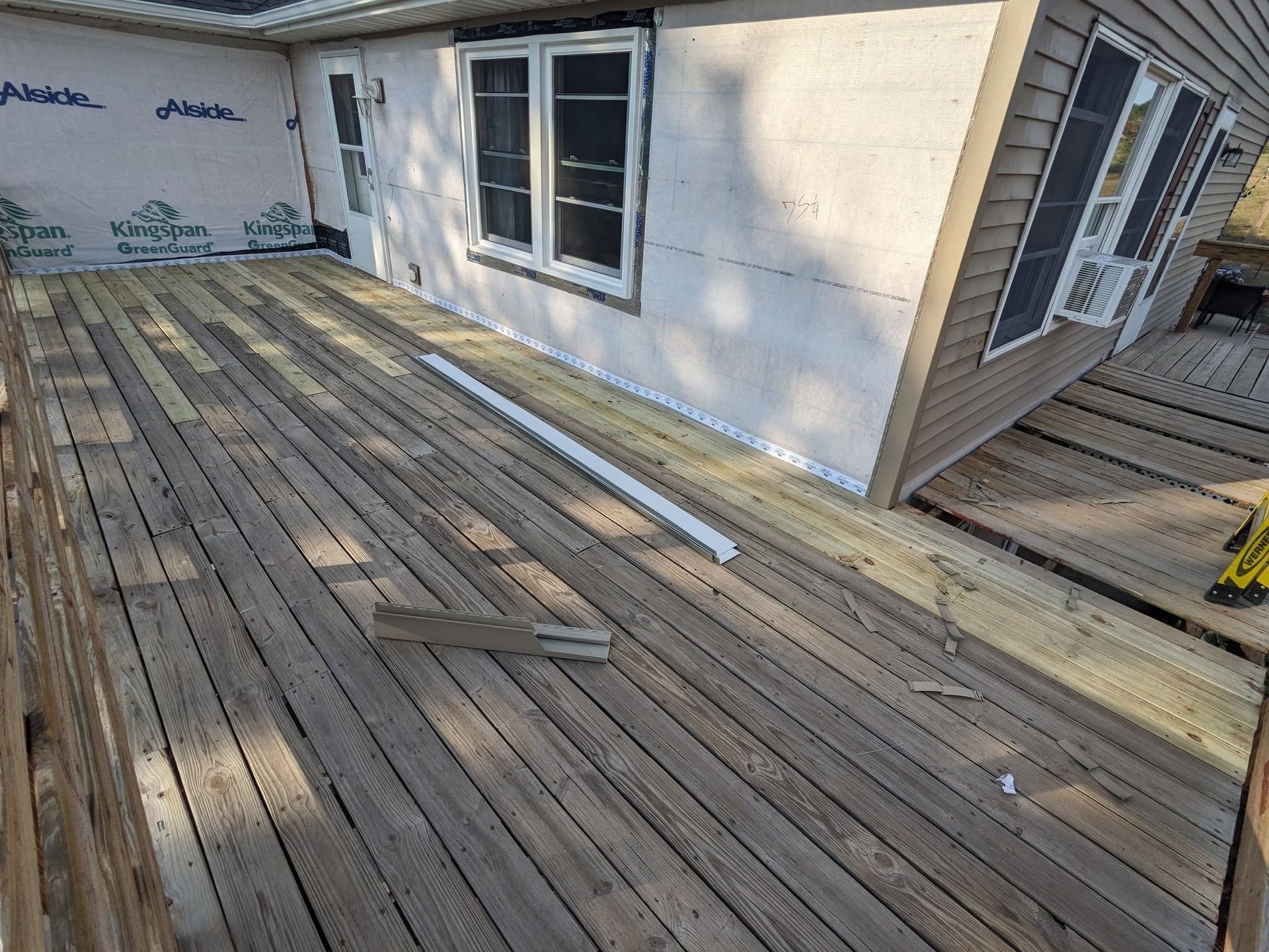 Deck under construction next to house, with siding, windows, and air conditioner.
