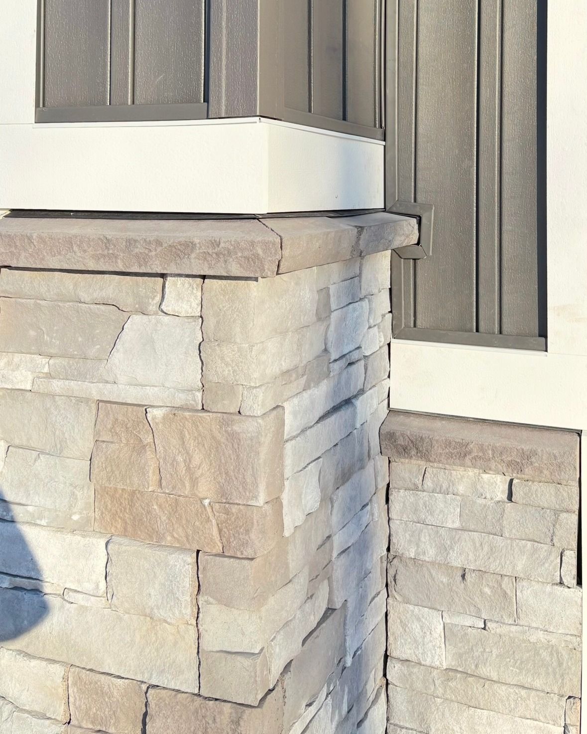Stone and wood facade corner: light-colored stone base, tan and grey wood siding, white trim.