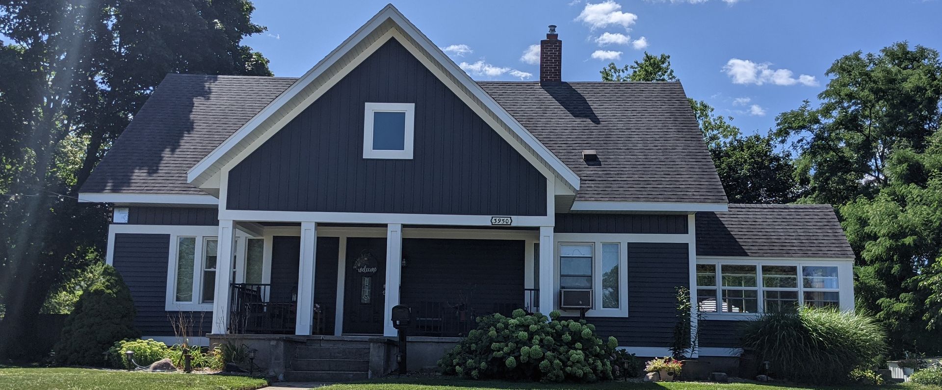 A dark blue house with white trim and a porch, a lawn, and a blue sky.
