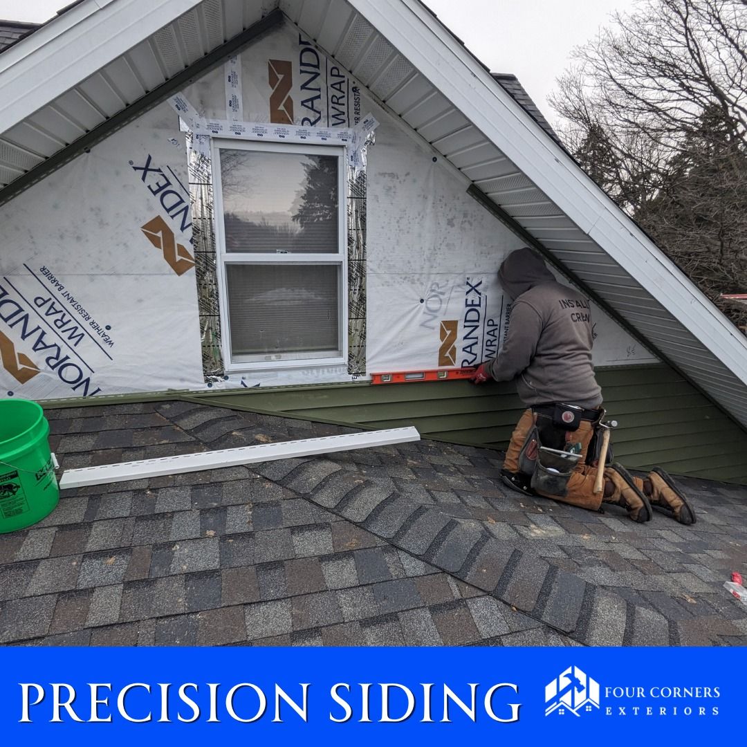 Person installing green siding on a house roof; using a level. White wrap, window, and a bucket visible.