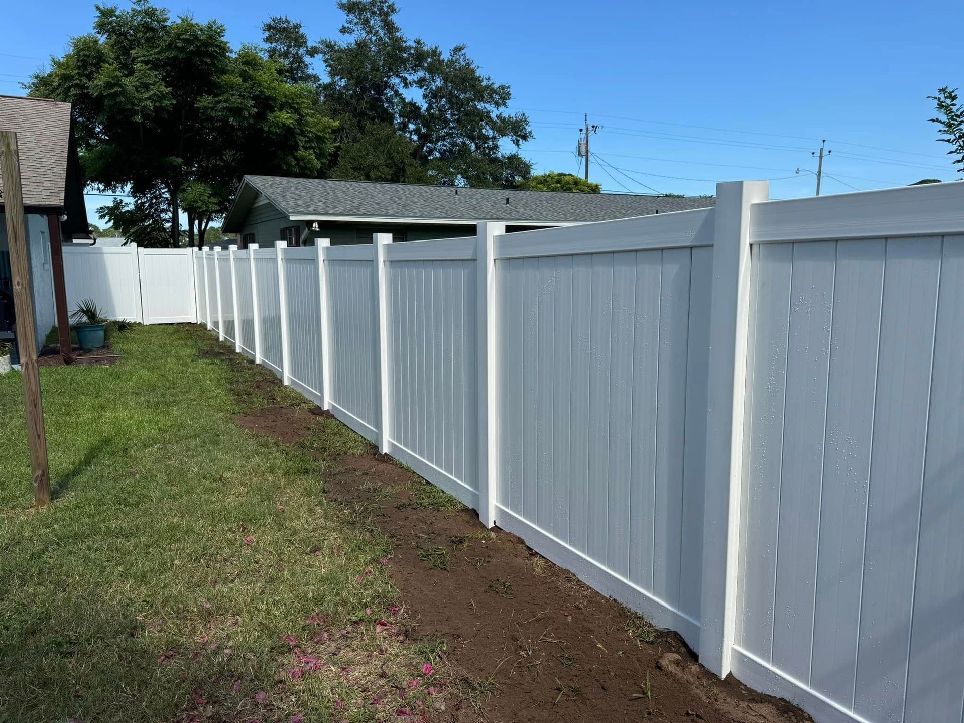 White vinyl fence along a grassy yard on a sunny day.