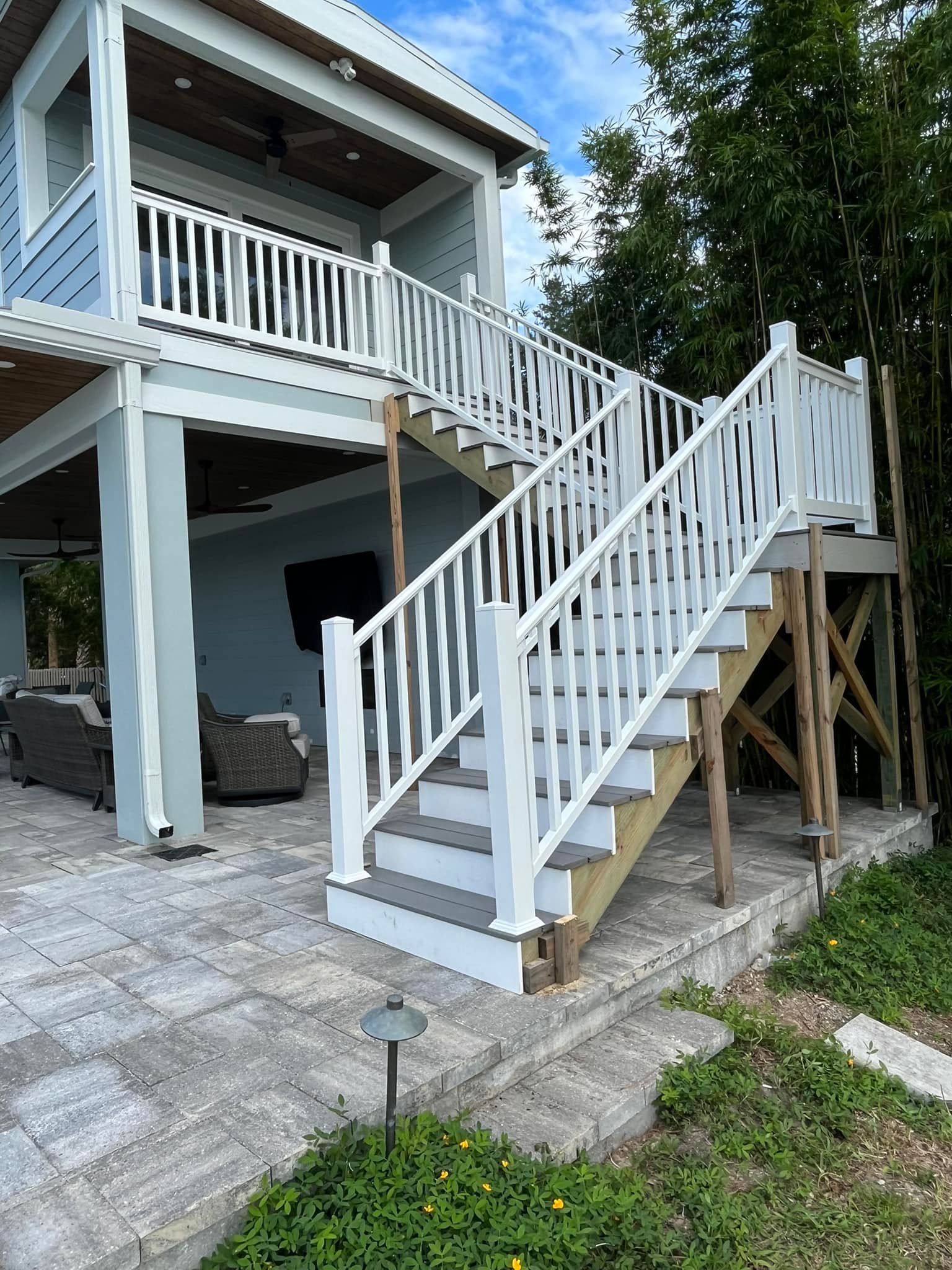 Exterior view of a two-story home with a white staircase, blue siding, and patio.