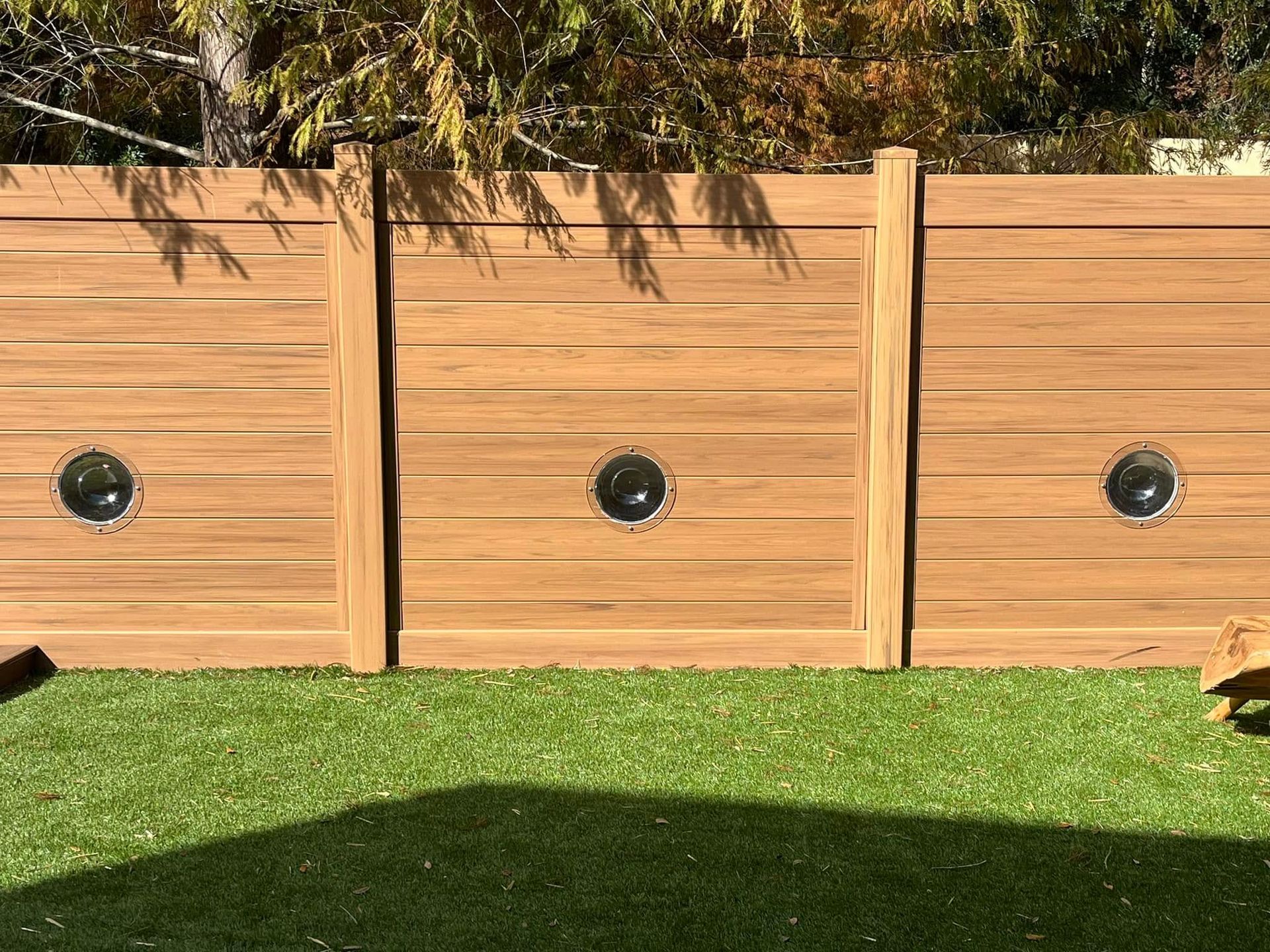 Wooden fence panels with porthole windows, set against a green lawn.