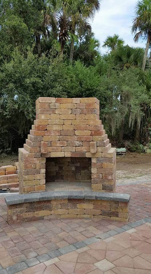 Brick outdoor fireplace with a raised hearth, in a backyard setting.