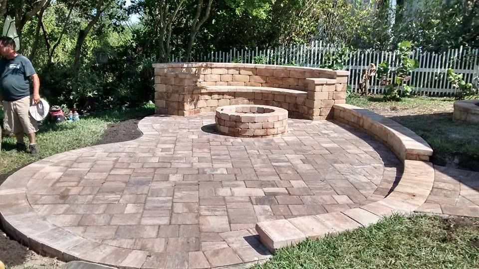 Brick patio with a built-in stone bench, fire pit, and curved border. Man stands at the side.