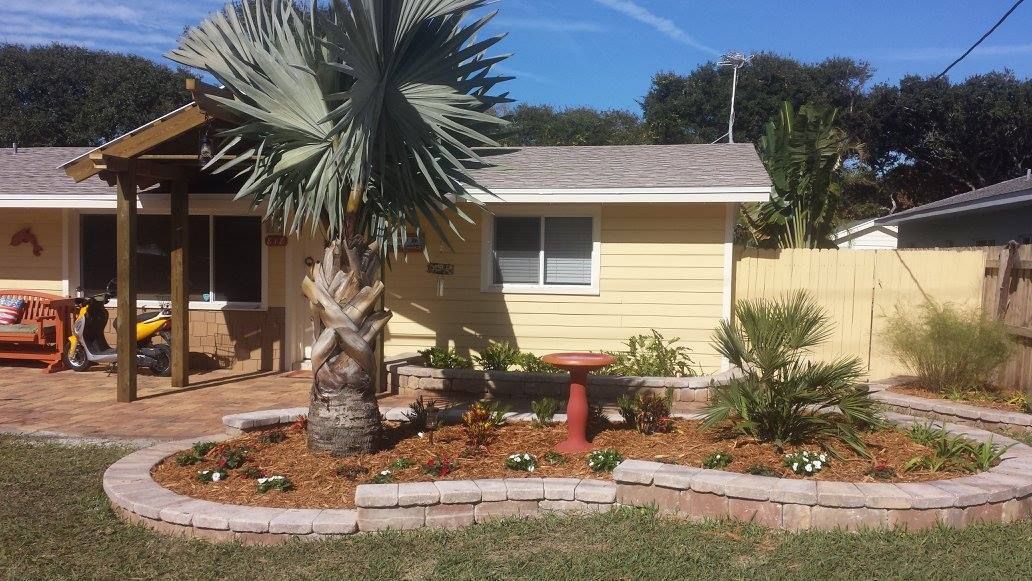 Yellow house with a small front yard garden, palm tree, and a bird bath.